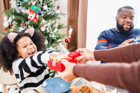 African American family surprising together with a gift on Christmas day while dinner. Merry Christmas. Happy family.の写真素材