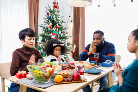 Families together to pray before meals at home. Celebration holiday togetherness near Christmas tree. African American family. Merry Christmas.の写真素材