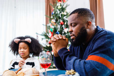 Families together to pray before meals at home. Celebration holiday togetherness near Christmas tree. African American family. Merry Christmas.の写真素材