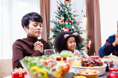 Families together to pray before meals at home. Celebration holiday togetherness near Christmas tree. African American family. Merry Christmas.の写真素材