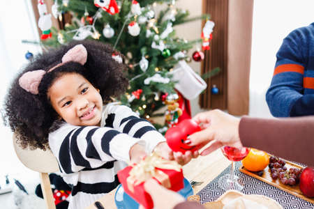 African American family surprising together with a gift on Christmas day while dinner. Merry Christmas. Happy family.の写真素材