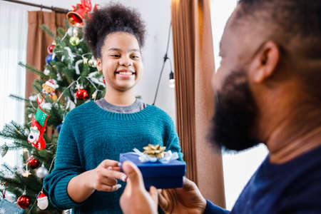 African American family surprising together with a gift on Christmas day while dinner. Merry Christmas. Happy family.の写真素材