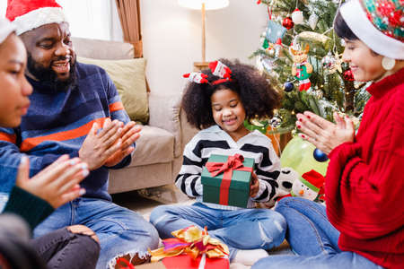 African American family surprising with a gift on Christmas day. Merry Christmas. Happy family.の写真素材
