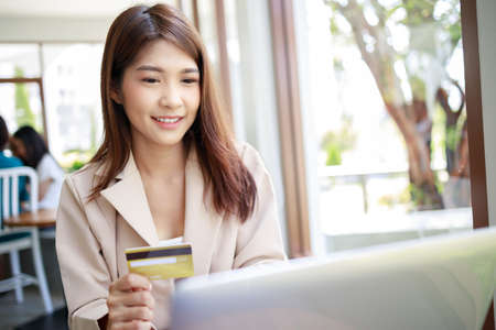 attractive Asian businesswoman using credit card for goods payments shopping online by laptop in the...
