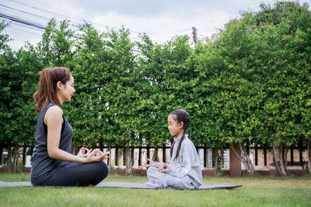 Family Asian Mother teacher training yoga child daughter on a yoga mat at home garden. Family outdoors. Parent with child spends time together. exercise at home concept and new normal.の写真素材