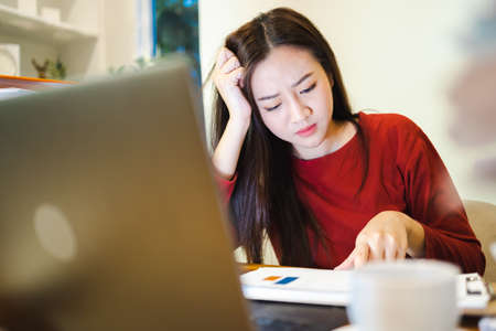 Workaholic people. Asian Stressed Elegant office lady checks reports  during overtime at homeの写真素材
