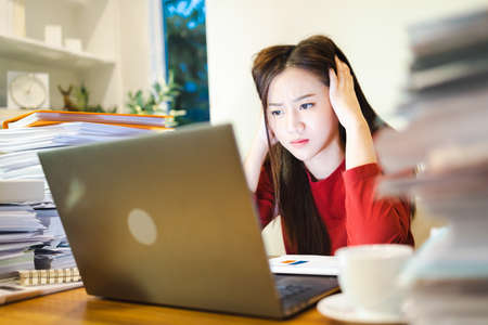Stressed freelancer checking reports and accounting in computer, working overtime at home officeの写真素材