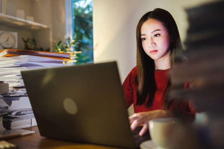 Asian businesswoman working on laptop computer at home office. work overtime doing deadline projectの写真素材