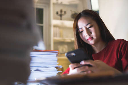 Busy Businesswoman using smartphone during overtime at home office. Busy people working.の写真素材