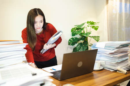 Woman doing overtime about urgent job and stand at desk at home at night. Workaholic people conceptの写真素材