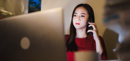 Freelancer woman using the phone during overtime working at the home officeの写真素材