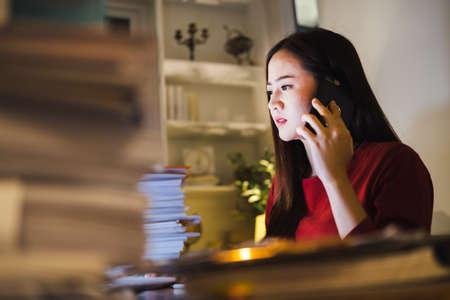 Busy Businesswoman talking business by phone during overtime at home office. Busy people working.の写真素材