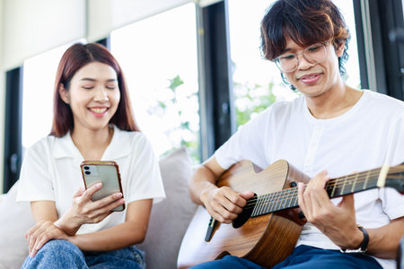 Happy couple at home, A Young man playing guitar to girlfriend in living room, Leisure activitiesの写真素材