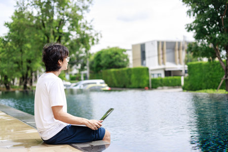 A man remote work during vacation working on his laptop near the swimming pool in resort hotel