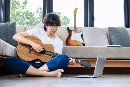 Young man playing guitar and learning a new song with laptop, guitarist musician lifestyleの写真素材