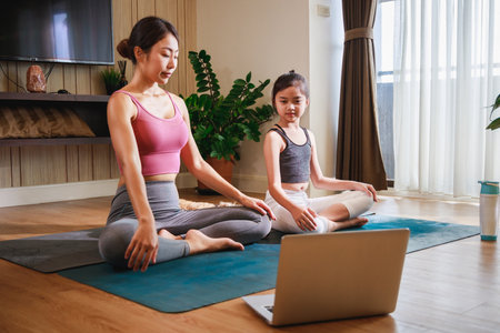 Asian woman and Little girl practicing yoga from yoga online course via laptop at homeの写真素材