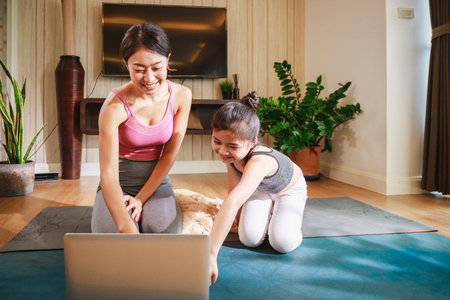 Asian woman and daughter practicing yoga from yoga online course via laptop at living homeの写真素材