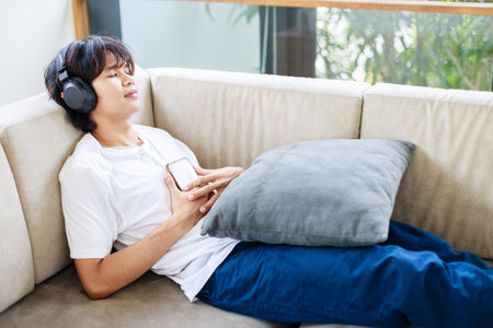 Asian Male using smartphone while listening to music at home. Time to relax and leisure activitiesの写真素材