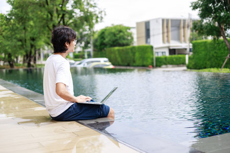 Digital Nomad in Casual Attire Completes Business Tasks Poolside on Vacationの写真素材
