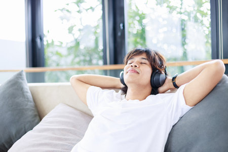Close-up of man listen to music on a comfortable couch at home. Time to relax and leisure activitiesの写真素材