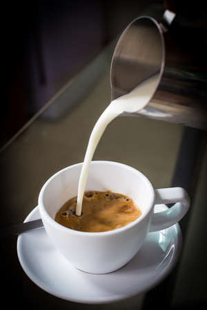 Pouring cream into a cup of coffeeの写真素材