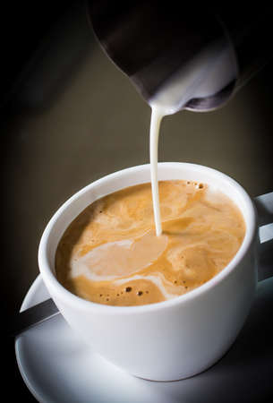 Pouring cream into a cup of coffeeの写真素材