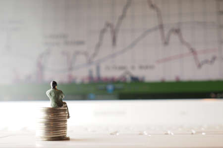 miniature businessman sitting on the coin looking the stock graphの写真素材