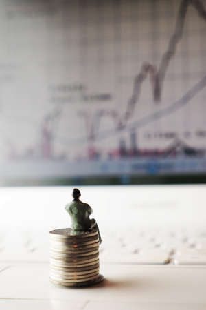 miniature businessman sitting on the coin looking the stock graphの写真素材