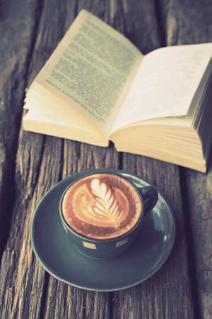 cup of coffee latte art on the wood desk and book in vintage color toneの写真素材