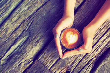 hand and cup of coffee latte art on the wood background vintage color toneの写真素材