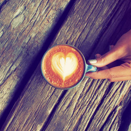 hand and cup of coffee latte art on the wood background vintage color toneの写真素材