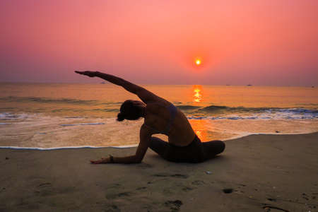 Silhouette young woman practicing yoga on the beach at sunriseの写真素材