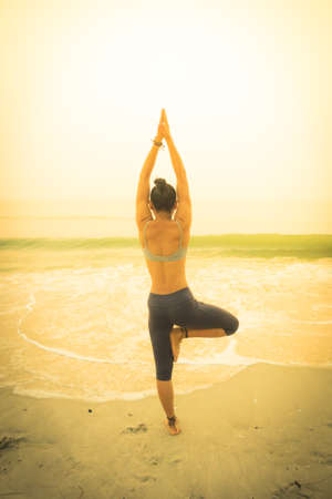 Silhouette young woman practicing yoga on the beach at sunriseの写真素材