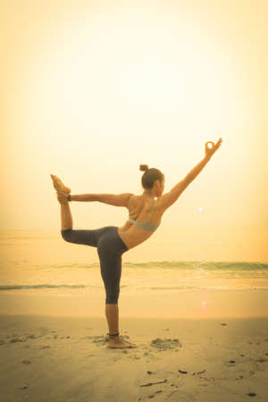 young woman practicing yoga on the beach at sunriseの写真素材