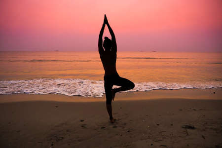 Silhouette young woman practicing yoga on the beach at sunriseの写真素材