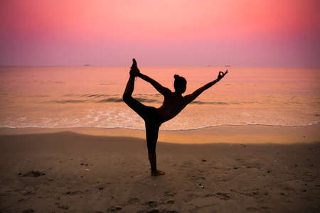 Silhouette young woman practicing yoga on the beach at sunriseの写真素材