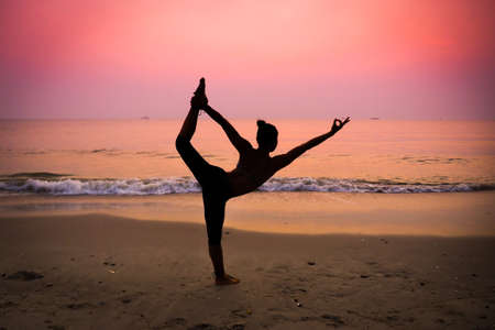Silhouette young woman practicing yoga on the beach at sunriseの写真素材