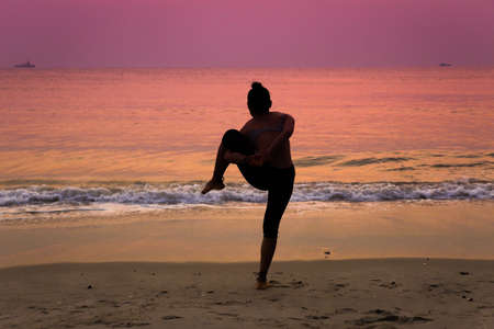 Silhouette young woman practicing yoga on the beach at sunriseの写真素材