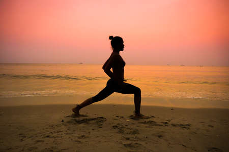 Silhouette young woman practicing yoga on the beach at sunriseの写真素材
