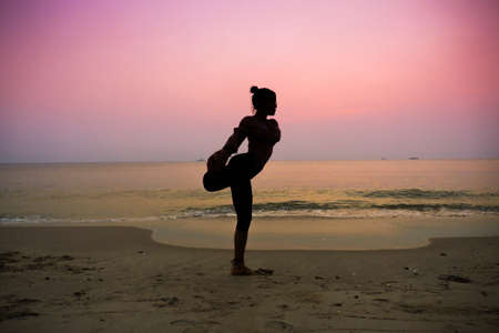 Silhouette young woman practicing yoga on the beach at sunriseの写真素材