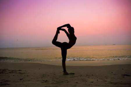 Silhouette young woman practicing yoga on the beach at sunriseの写真素材