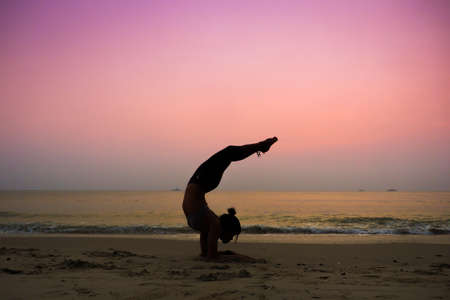 Silhouette young woman practicing yoga on the beach at sunriseの写真素材