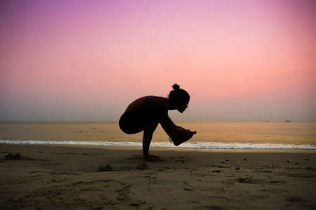 Silhouette young woman practicing yoga on the beach at sunriseの写真素材