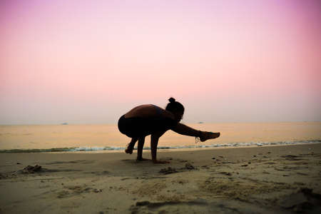 Silhouette young woman practicing yoga on the beach at sunriseの写真素材