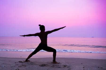 Silhouette young woman practicing yoga on the beach at sunriseの写真素材