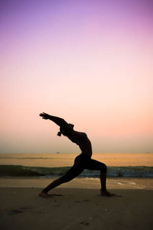 Silhouette young woman practicing yoga on the beach at sunriseの写真素材