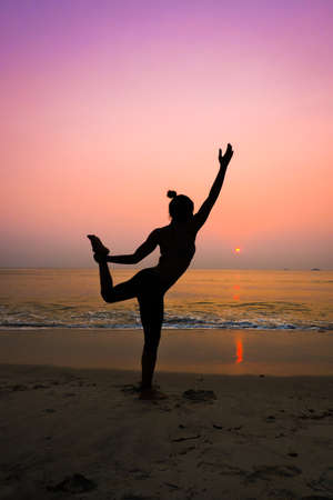 Silhouette young woman practicing yoga on the beach at sunriseの写真素材