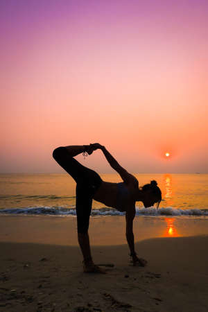Silhouette young woman practicing yoga on the beach at sunriseの写真素材