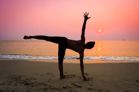 Silhouette young woman practicing yoga on the beach at sunriseの写真素材