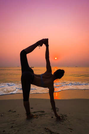 Silhouette young woman practicing yoga on the beach at sunriseの写真素材